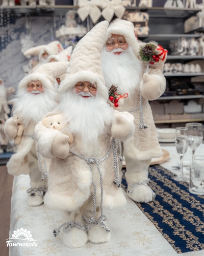 Figurines de Pères Noël en costumes blancs sur une table décorée.